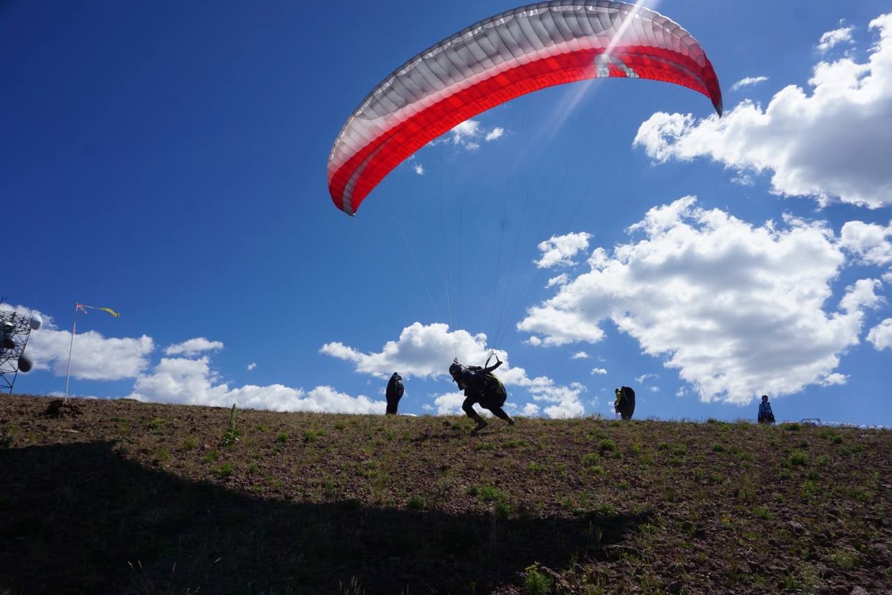 Paraglider launching from a grassy ridge during the Red Rocks Skills Fly-In in Monroe, Utah
